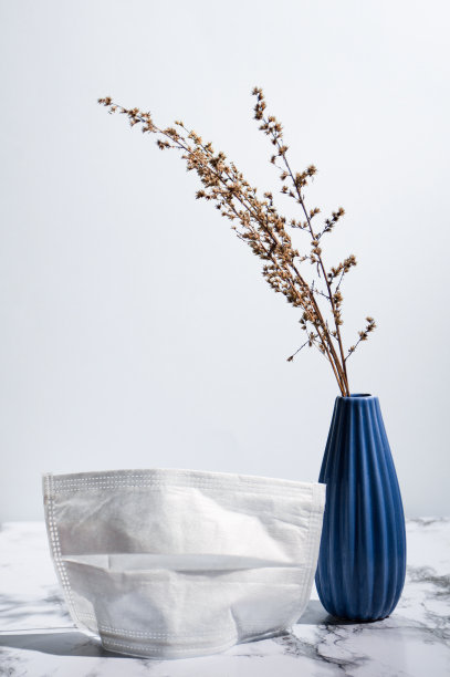 极简主义的照片，深蓝色花瓶与干燥的植物和手术面具在大理石表面上的光背景图片下载