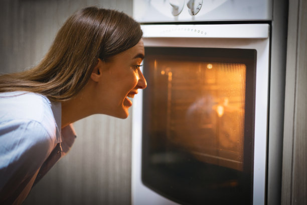 快乐的年轻女子在厨房看烤箱图片下载