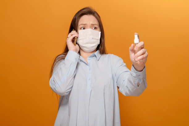 冠状病毒大流行，特写照片中的年轻女子在黄色背景下打电话，惊慌失措，手里拿着杀菌剂喷雾图片下载