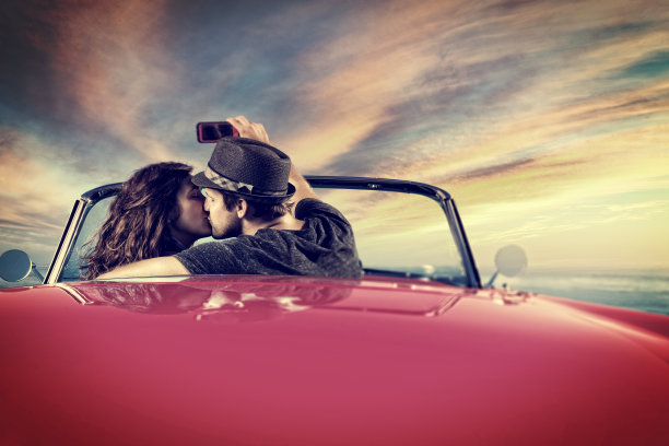 一对情侣在敞篷车里拍摄日落自拍图片下载