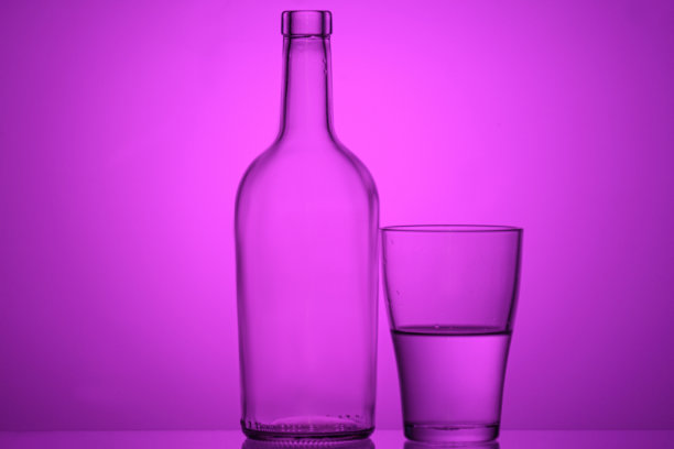 一个瓶子和半满的玻璃与背光在紫色背景的照片图片下载