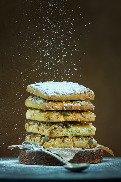 带有坚果和种子的方形饼干在棕色的背景上撒上糖粉。有拷贝空间的照片。图片下载