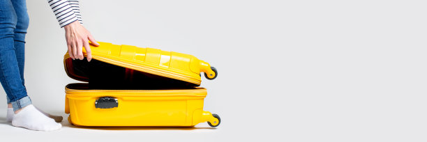 一个年轻女子打开一个手提箱，背景很亮。度假和旅行的概念。横幅图片下载