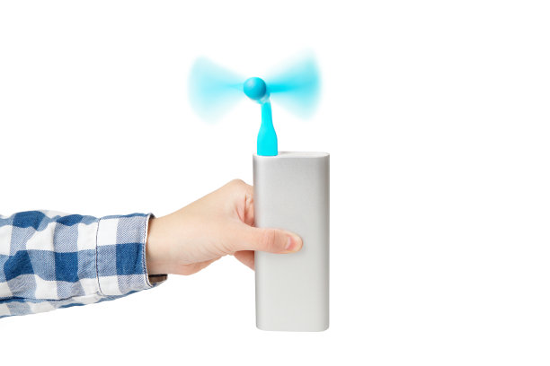 女性的手，穿着长袖格子衬衫，拿着一个旋转的便携式usb风扇，连接着一个银色的电源隔离在白色。图片下载