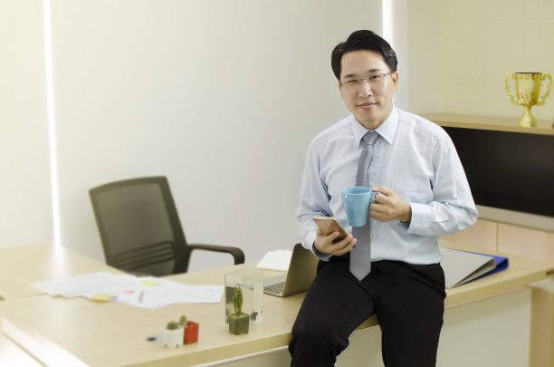 专业商人端着一杯咖啡，微笑的坐在桌子上图片下载