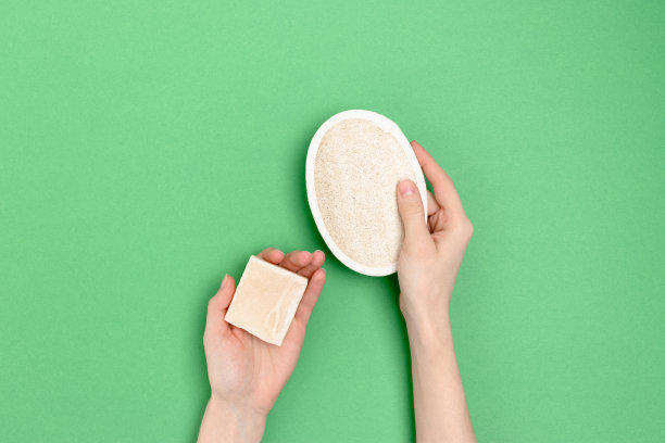 女性手里拿着手工肥皂和丝瓜海绵。绿色背景上的极简构图。图片下载