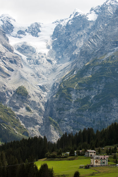 冰冷的岩石山脉覆盖着冰雪，覆盖着绿色的山谷，山谷之间有冷杉树和房屋。图片下载