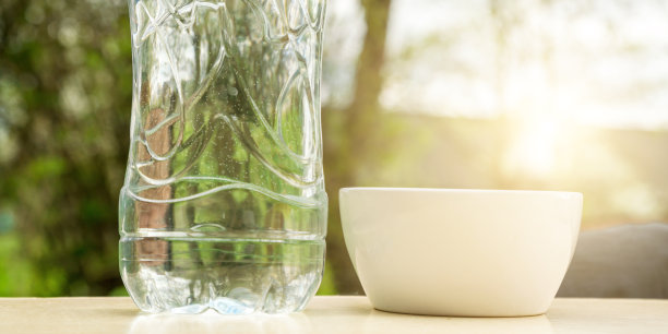 阳光下花园桌上的塑料瓶旁边的白色杯子图片下载