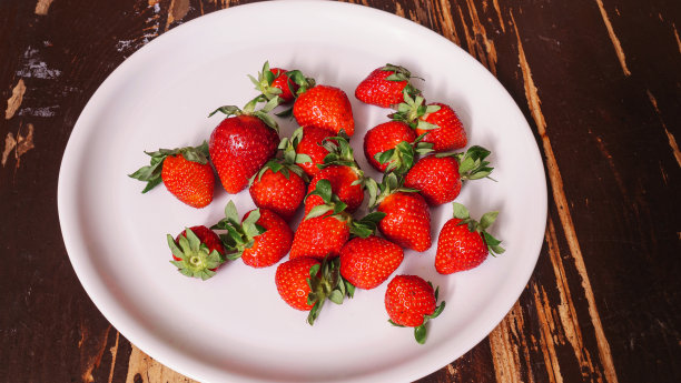 木桌上的白盘子里装着许多成熟的红草莓。从以上观点。图片下载