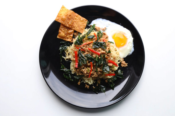 麻辣方便面，圣罗勒叶，猪肉末和脆皮饺子装在一个黑色的盘子里图片下载