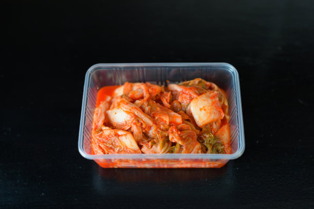 传统韩国食品泡菜在塑料容器中水平拍摄，以黑色为背景图片下载