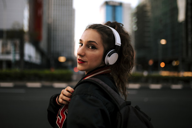 美丽的西班牙女人听音乐耳机和智能手机在户外。在城市背景下穿着运动服的拉丁女孩。图片下载