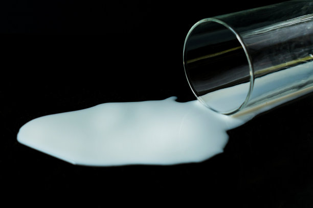 一杯洒在黑色背景上的牛奶。图片下载