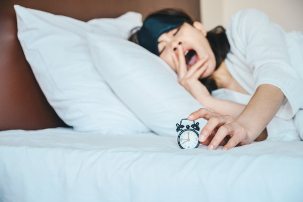 一个昏昏欲睡的女人试图按下闹钟按钮停止声音时，闹钟提醒从他们的晚上的睡眠或短暂的小睡。图片下载