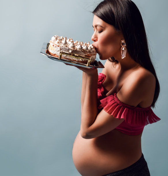 年轻美丽的孕妇在粉红色的顶部吃美味的奶油蛋糕肖像图片下载