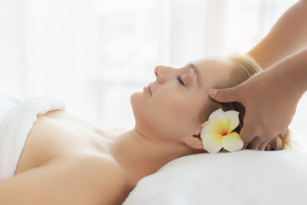 美丽的年轻女子享受水疗沙龙在豪华度假村或酒店。客户在水疗室接受面部按摩，让她缓解压力东方按摩师按摩客户头部素材图片