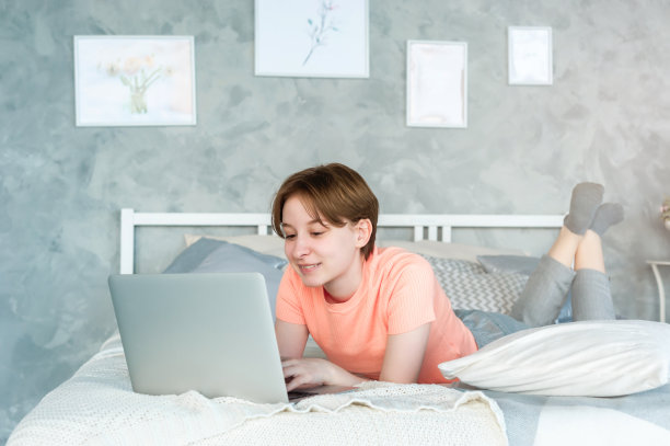 一个十几岁的女孩正躺在床上，手里拿着笔记本电脑，微笑着看着屏幕图片下载