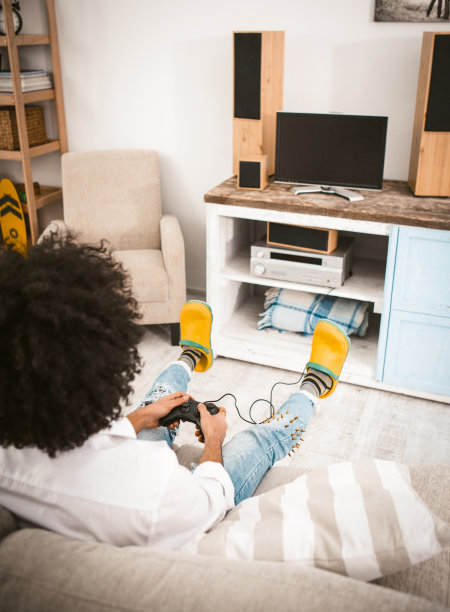 年轻男人在家中沙发上玩电脑游戏，背对电视图片下载