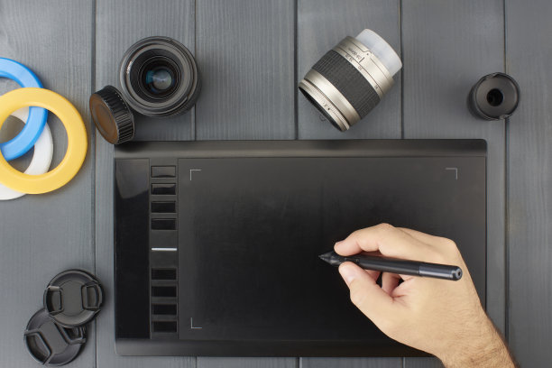 用白色的人手和笔在灰色的木头上进行图形设计的写字板，带有照相机镜头和滤色镜图片下载