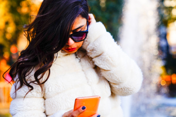 漂亮的黑发女人在公园里看手机。社交媒体和技术图片下载