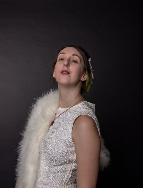 一个年轻迷人优雅的白人女人的复古照片与棕色深褐色的头发和突出的绿色头发，穿着性感的白色连衣裙和皮草包裹在黑色的背景。图片下载