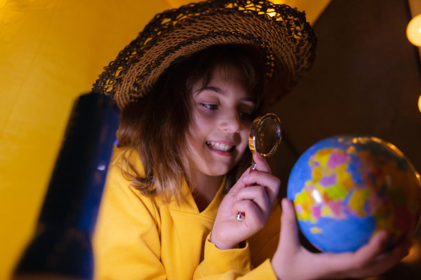 年轻的女孩学生在一个家庭制作的帐篷里学习和家庭教育发光的球。图片下载