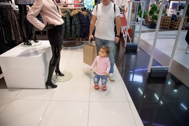 黑色星期五促销理念，带孩子购物。可爱的小女孩站在服装店的模特面前。后面是爸爸拿着一个纸袋去购物。特写，软焦点，模糊背景图片下载