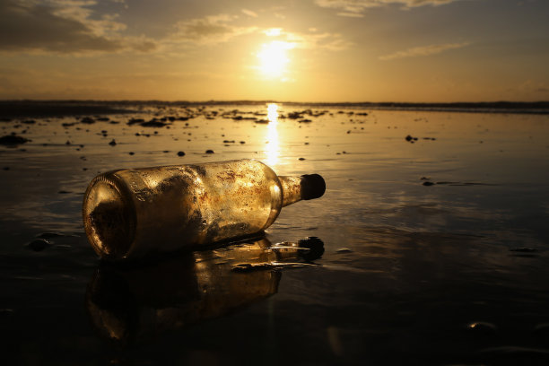 海滩上的瓶中信。美丽的日落和阳光在沙滩上的反射图片下载