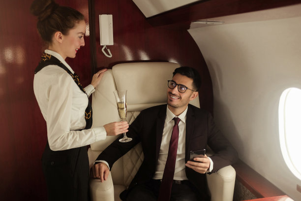 男亿万富翁乘坐私人飞机，接听电话，接待给他端来香槟的空姐，在飞机上享受商务旅行图片下载