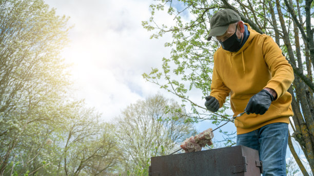 戴手套的老人把烤肉串放在花园烤架上图片下载