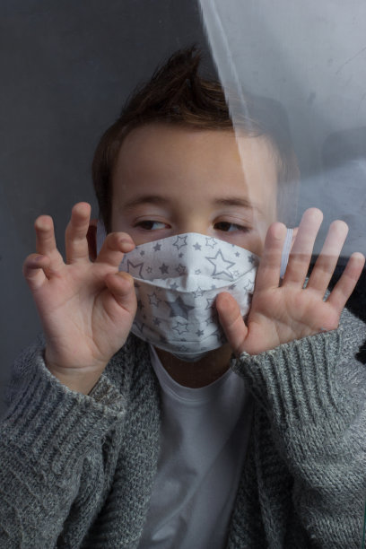 男孩戴着医用面罩，透过玻璃看，手放在他身上。疫情期间的隔离和自我隔离概念图片下载