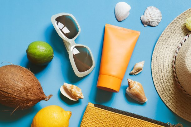 夏美平躺着照片。化妆包，防晒霜管，椰子，柠檬，酸橙，太阳帽和贝壳在蓝色的背景。海滩必需品图片下载