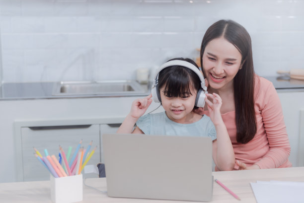 美丽的亚洲女性妈妈和女孩们在网上学习在家里通过笔记本电脑通过耳机听声音在家人的支持下。素材图片