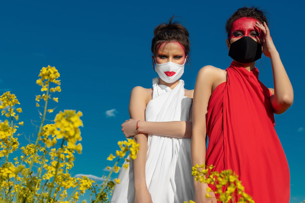 两个漂亮的年轻的黑发女孩与创意明亮的妆容在束腰外衣在蓝天面具图片下载