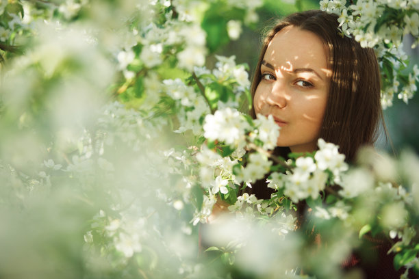 一个皮肤干净的年轻女子站在一棵盛开的苹果树旁。温柔的女孩肖像在春天的公园。图片下载