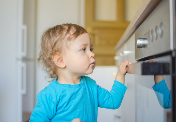 一个好奇的小孩在厨房里玩烤箱的把手。危险无人看管儿童，事故预防在家概念照片图片下载