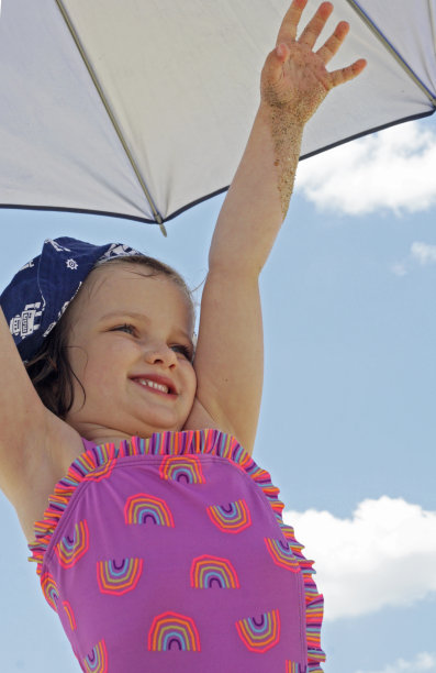 一个在伞下穿着彩虹泳衣的微笑小女孩。图片下载