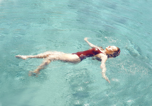 快乐的女孩在泳池里游泳。俯视图的一个女孩在游泳池，一个时尚的女孩在红色泳衣放松。旅行，休息，阳光，夏天。图片下载