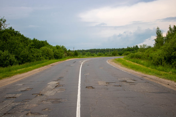 绿色森林中间的一条弯曲的旧公路。夏天的一天。图片下载