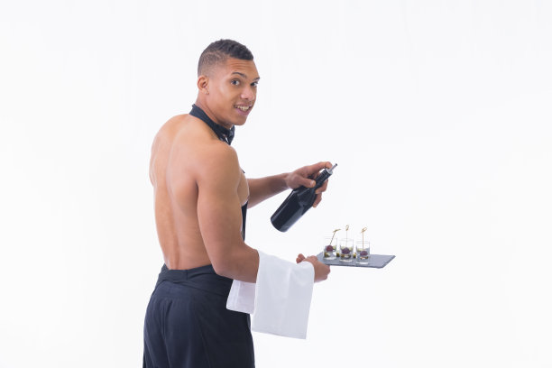 微笑的年轻侍者拿着一个瓶子，一条毛巾和一个有玻璃杯的盘子图片下载