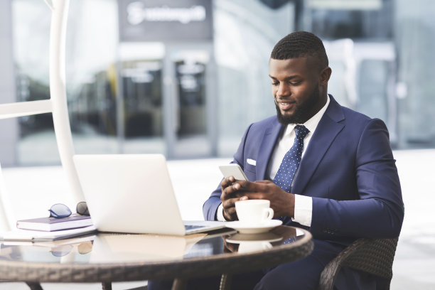 商人用手机工作在笔记本电脑坐在户外咖啡馆图片下载