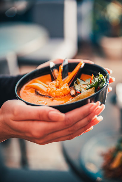 泛亚洲食品。女人手里拿着黑碗里的冬阴汤图片下载