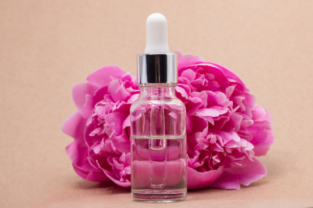 美容产品化妆品血清米色背景旁边的新鲜牡丹花。粉红色的牡丹花在米色背景上。图片下载