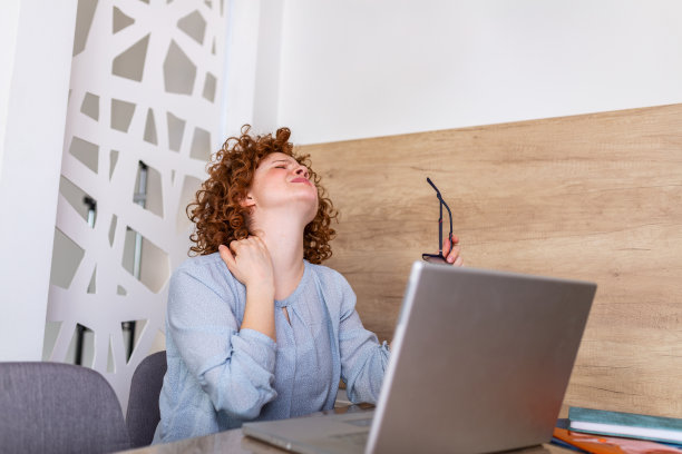 女商人觉得脖子痛后，坐在桌子上的笔记本电脑。因长时间在电脑上工作而患上“办公室综合症”的疲惫女性。漂亮女孩在按摩她紧张的颈部肌肉图片下载