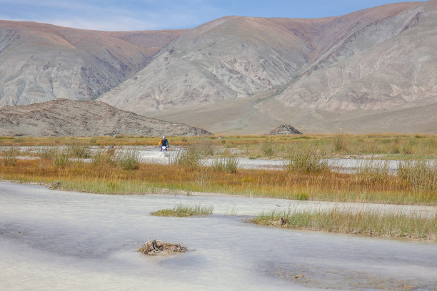 一个骑摩托车的人正骑着摩托车穿越白色的山河。山阿尔泰,蒙古。图片下载