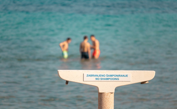 在bacvice海滩上的公共淋浴，并有一个警告标志，禁止在公共场合使用洗发水。远处沙滩上的人们图片下载