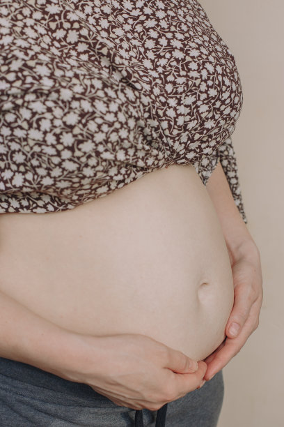 一个孕妇的肚子的特写。一个怀孕的女孩站在米色的背景上，用手捂着肚子图片下载