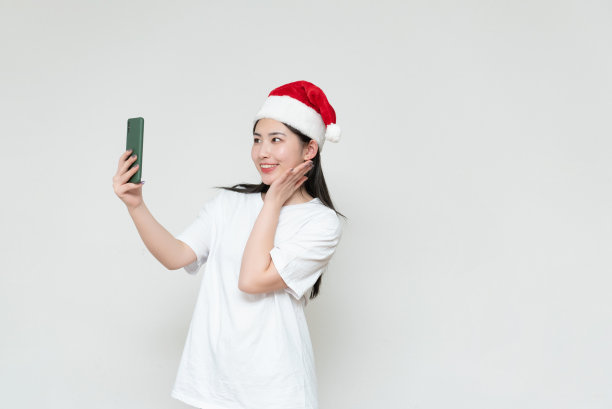 一位戴着圣诞帽的年轻亚洲妇女站在白墙前图片下载