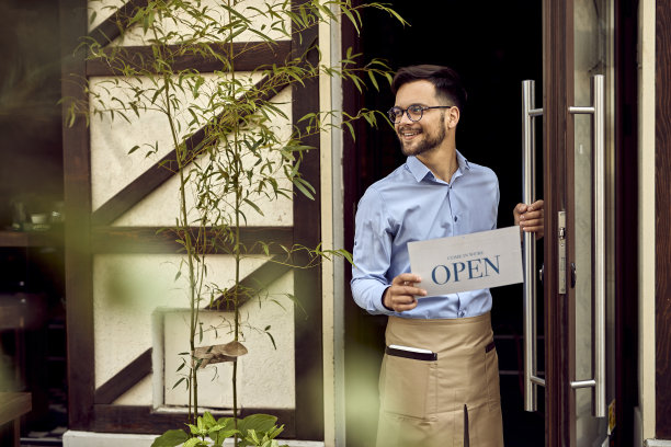 快乐的侍者在咖啡馆门口挂着开门的牌子。图片下载