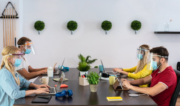 在共同工作创意办公室工作的年轻人，戴着预防冠状病毒传播的防护口罩——社交距离、科技和创业理念——关注左女性脸图片下载